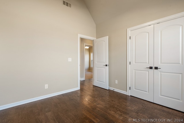 unfurnished bedroom with high vaulted ceiling, dark hardwood / wood-style floors, and a closet