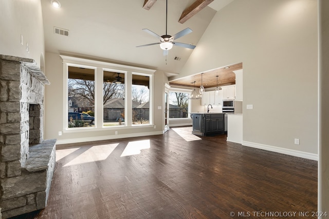 unfurnished living room featuring high vaulted ceiling, ceiling fan with notable chandelier, beamed ceiling, a stone fireplace, and dark hardwood / wood-style flooring