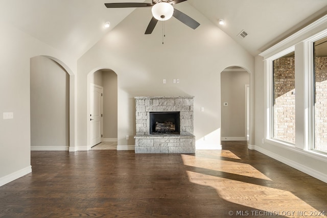 unfurnished living room featuring ceiling fan, dark hardwood / wood-style floors, high vaulted ceiling, and a stone fireplace