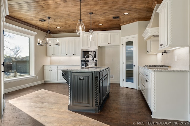 kitchen featuring pendant lighting, white cabinets, backsplash, custom range hood, and a center island with sink