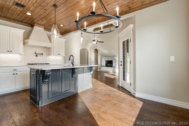 kitchen featuring dark hardwood / wood-style floors, an island with sink, a fireplace, premium range hood, and a kitchen bar