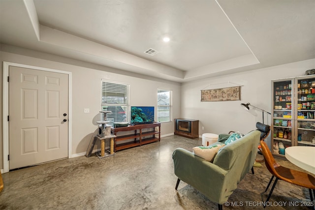 living room with finished concrete flooring, baseboards, visible vents, and a raised ceiling