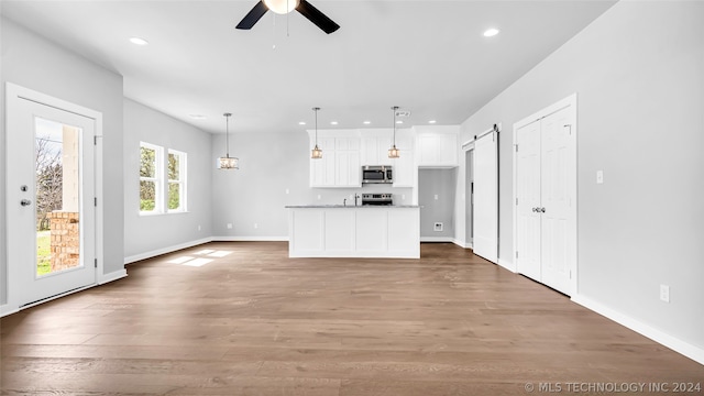 unfurnished living room with a barn door, ceiling fan, and wood-type flooring