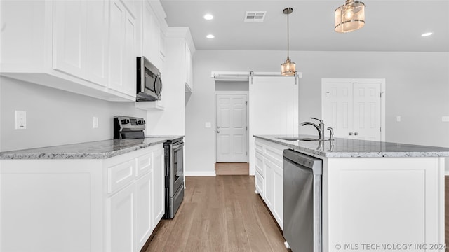 kitchen with appliances with stainless steel finishes, a kitchen island with sink, hardwood / wood-style floors, and white cabinetry