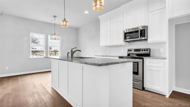 kitchen with appliances with stainless steel finishes, dark stone countertops, light hardwood / wood-style floors, white cabinetry, and a center island with sink