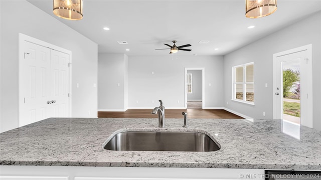 kitchen featuring dark wood-type flooring, light stone counters, ceiling fan, and sink