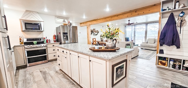 kitchen with a center island, stainless steel appliances, light stone counters, and light wood-type flooring