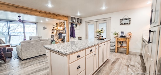 kitchen with light stone counters, a center island, light hardwood / wood-style flooring, and white cabinetry