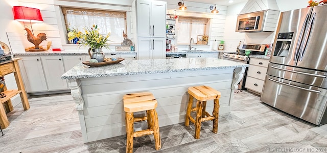 kitchen featuring sink, a kitchen island, stainless steel appliances, light stone counters, and a breakfast bar