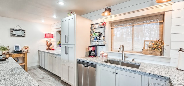 kitchen with light stone counters, sink, light hardwood / wood-style floors, and dishwasher