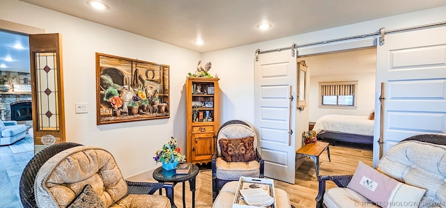 living area featuring a stone fireplace, a barn door, and light hardwood / wood-style flooring