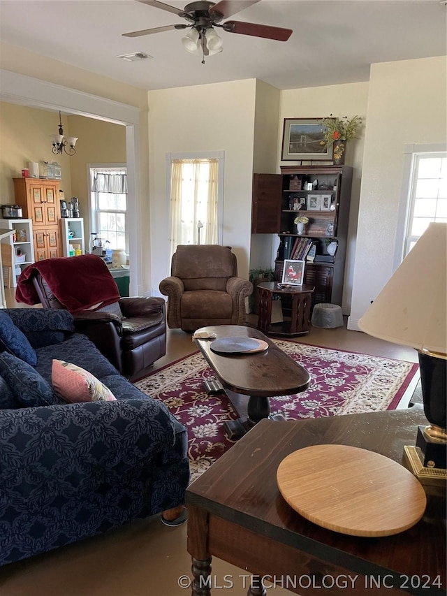 living room featuring plenty of natural light, visible vents, and ceiling fan with notable chandelier