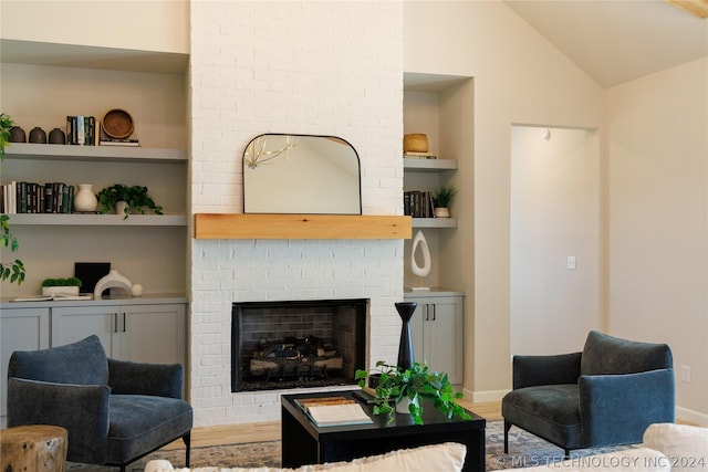 living room with built in shelves, hardwood / wood-style flooring, lofted ceiling, and a brick fireplace