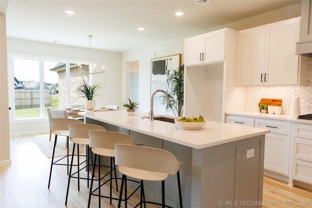 kitchen with tasteful backsplash, sink, pendant lighting, white cabinetry, and an island with sink