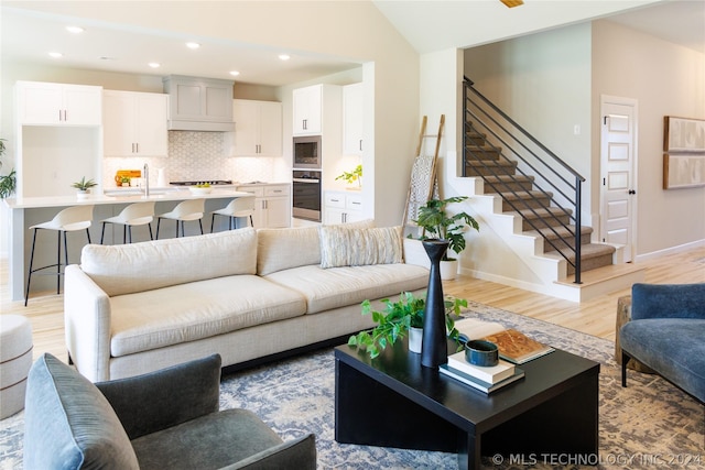 living room featuring light wood-type flooring, vaulted ceiling, and sink