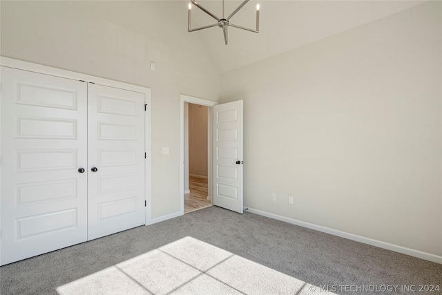 unfurnished bedroom with a chandelier, light colored carpet, high vaulted ceiling, and a closet