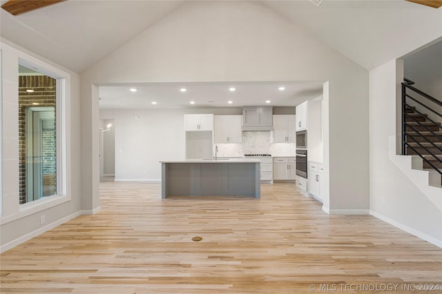 kitchen with premium range hood, a kitchen island with sink, sink, tasteful backsplash, and light hardwood / wood-style floors