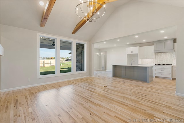 unfurnished living room featuring a chandelier, beam ceiling, light hardwood / wood-style floors, and sink