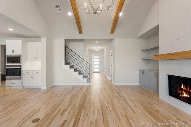 unfurnished living room featuring vaulted ceiling with beams, an inviting chandelier, light wood-type flooring, and a brick fireplace