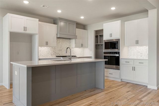 kitchen with backsplash, white cabinets, light hardwood / wood-style flooring, an island with sink, and stainless steel appliances