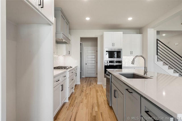 kitchen with backsplash, sink, gray cabinets, light wood-type flooring, and appliances with stainless steel finishes