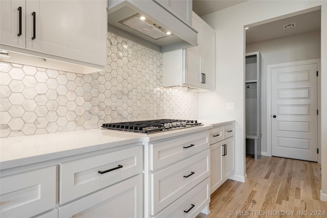 kitchen featuring exhaust hood, white cabinets, light wood-type flooring, tasteful backsplash, and stainless steel gas cooktop