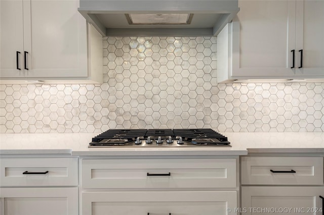 kitchen featuring decorative backsplash, premium range hood, white cabinets, and stainless steel gas stovetop