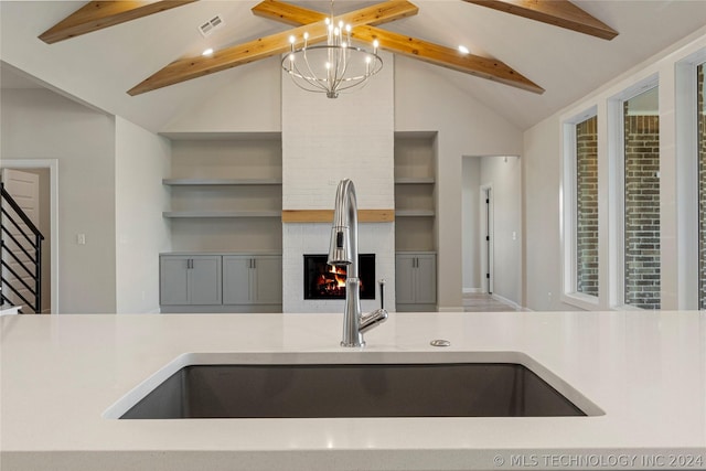 kitchen with a brick fireplace, sink, lofted ceiling with beams, built in features, and an inviting chandelier