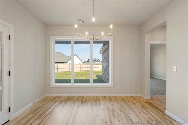 unfurnished dining area featuring plenty of natural light, light hardwood / wood-style floors, and a chandelier