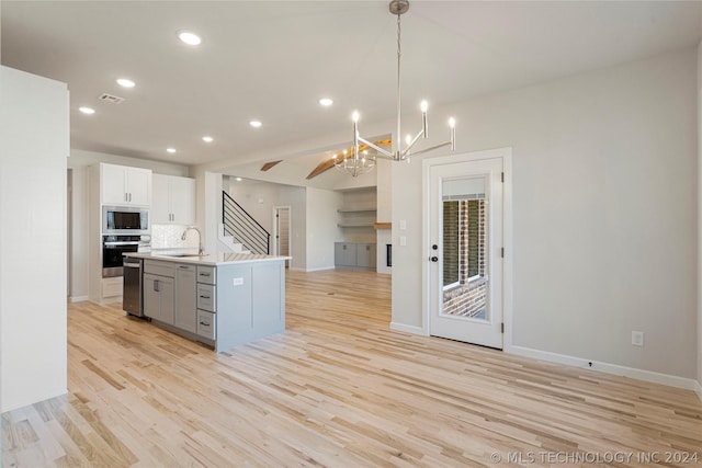 kitchen featuring hanging light fixtures, stainless steel appliances, tasteful backsplash, a center island with sink, and white cabinets