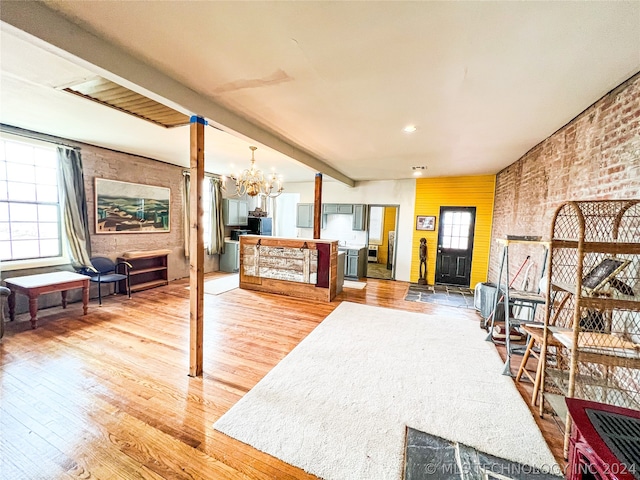 interior space with brick wall, a notable chandelier, light wood-type flooring, and beam ceiling