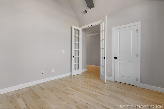 empty room with french doors, vaulted ceiling, and light hardwood / wood-style flooring