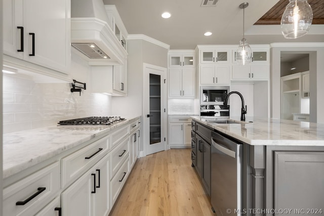 kitchen with hanging light fixtures, sink, white cabinets, custom range hood, and tasteful backsplash