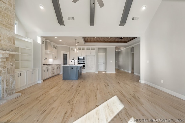 kitchen with pendant lighting, light wood-type flooring, an island with sink, wall chimney exhaust hood, and white cabinets