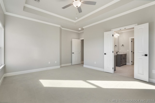 unfurnished bedroom featuring light carpet, ensuite bathroom, ceiling fan, ornamental molding, and a tray ceiling