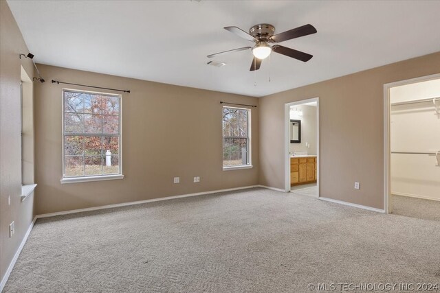 unfurnished bedroom featuring a closet, ensuite bathroom, ceiling fan, a walk in closet, and light carpet