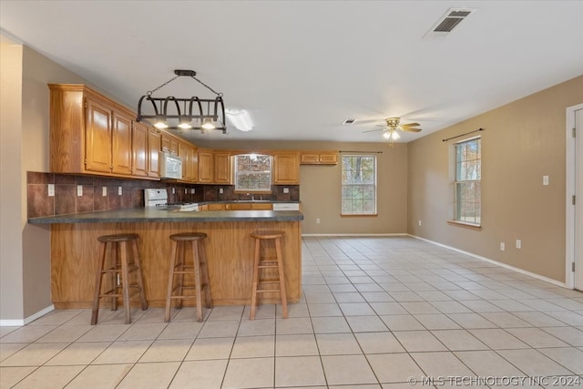 kitchen with white appliances, kitchen peninsula, tasteful backsplash, light tile flooring, and ceiling fan