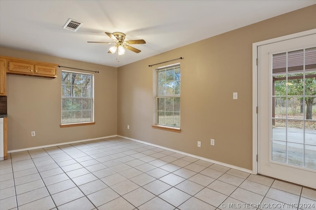 empty room with a healthy amount of sunlight, ceiling fan, and light tile floors