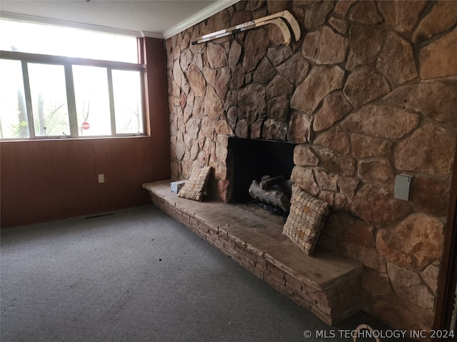 unfurnished living room featuring dark carpet, ornamental molding, and a stone fireplace