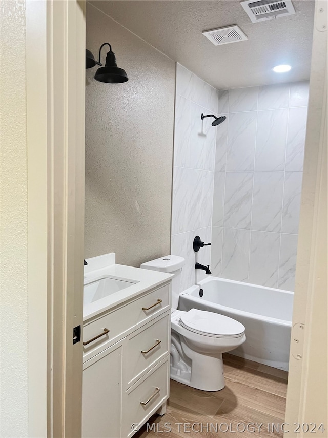 full bathroom featuring a textured ceiling, hardwood / wood-style floors, tiled shower / bath combo, vanity, and toilet