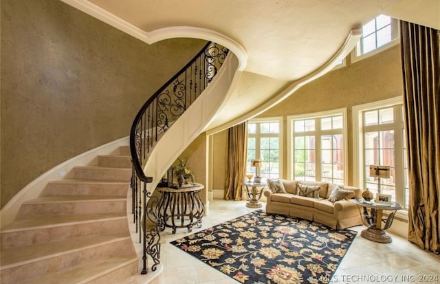 stairs featuring crown molding, a towering ceiling, light tile floors, and a healthy amount of sunlight