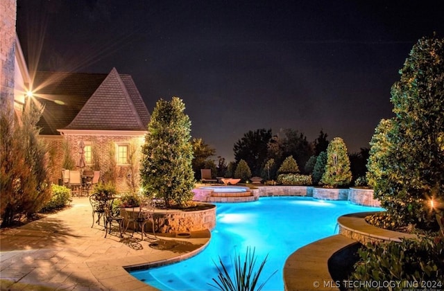 pool at night featuring an in ground hot tub and a patio area