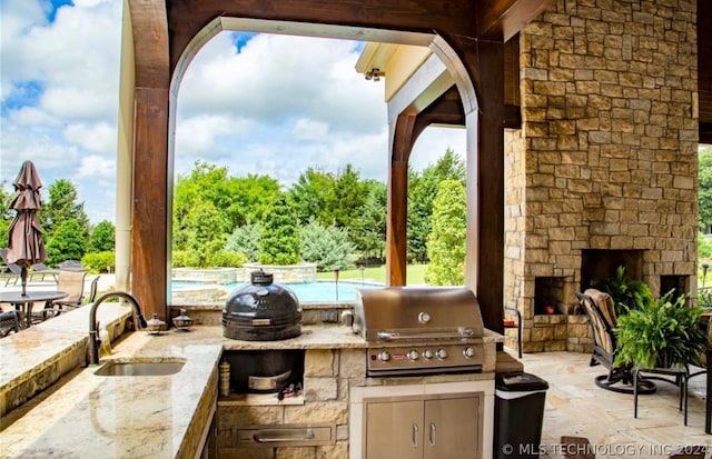 view of terrace featuring area for grilling, sink, grilling area, and an outdoor stone fireplace