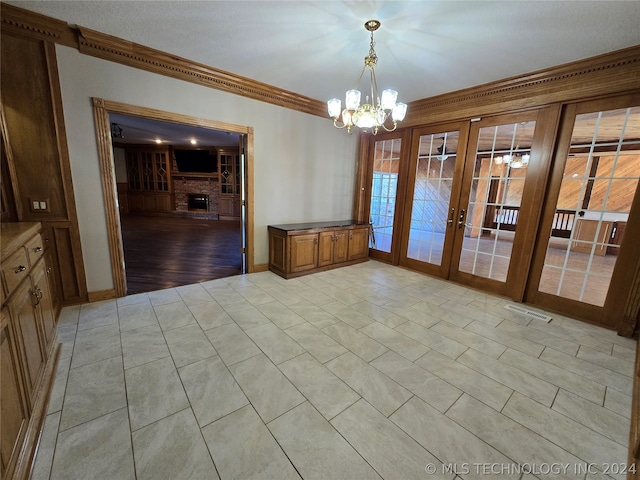 unfurnished dining area with french doors, crown molding, a chandelier, a fireplace, and light tile floors