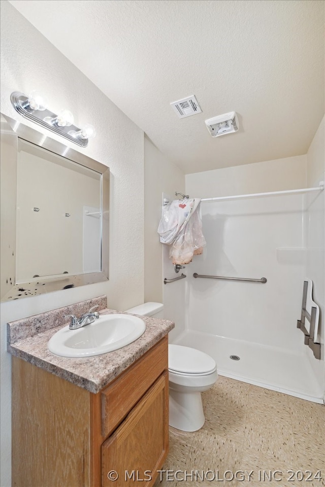 bathroom featuring a shower, tile floors, large vanity, toilet, and a textured ceiling