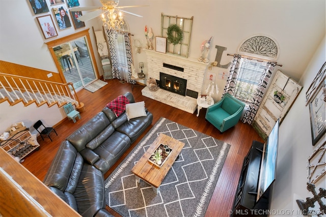 living room featuring dark hardwood / wood-style flooring, a brick fireplace, ceiling fan, and a high ceiling