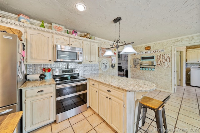 kitchen featuring appliances with stainless steel finishes, light tile flooring, a breakfast bar area, decorative light fixtures, and washer / clothes dryer