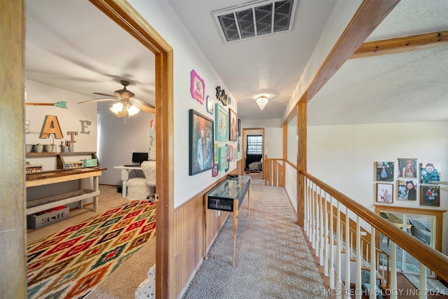 hallway with light colored carpet, beam ceiling, and a textured ceiling