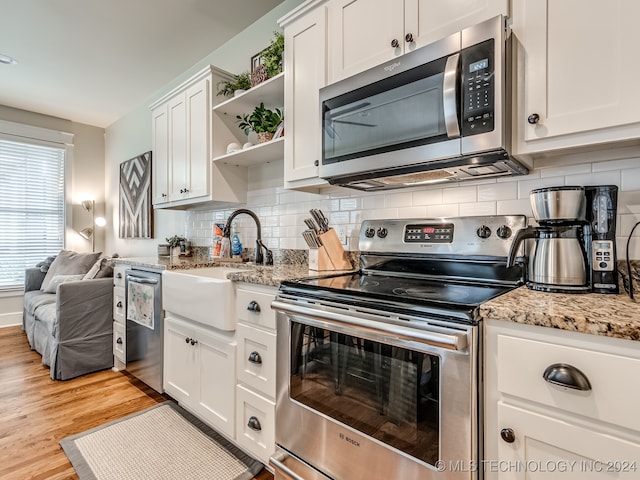 kitchen with tasteful backsplash, sink, stainless steel appliances, white cabinets, and light hardwood / wood-style flooring