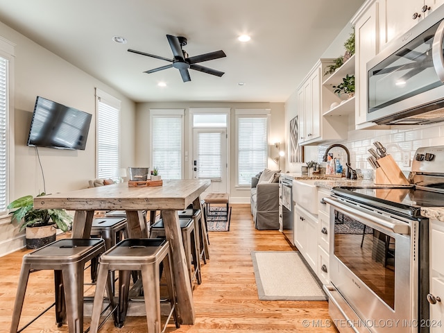 kitchen with light hardwood / wood-style flooring, backsplash, light stone countertops, white cabinets, and appliances with stainless steel finishes